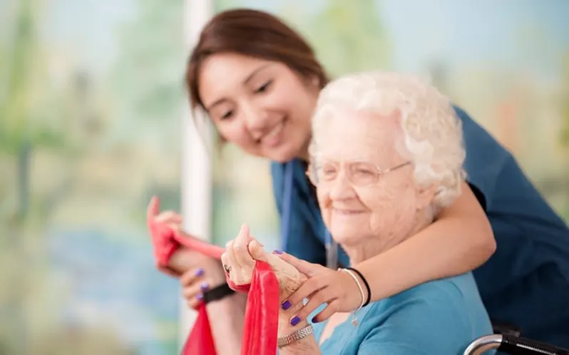 Caregiver assisting elderly woman with resistance band exercise