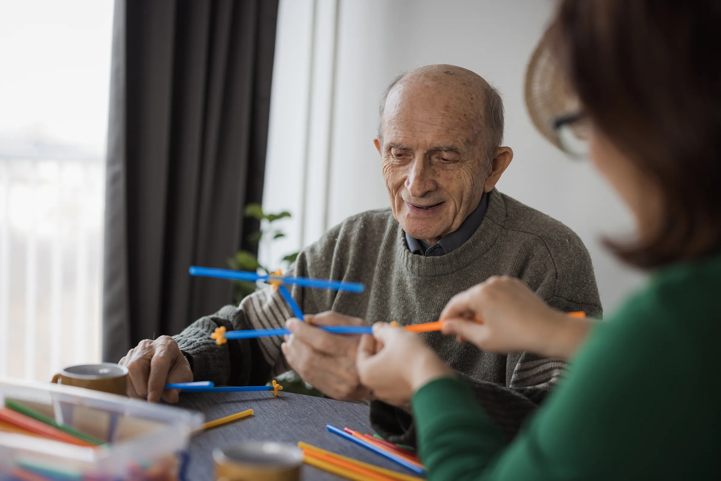 Elderly man building with colorful sticks indoors