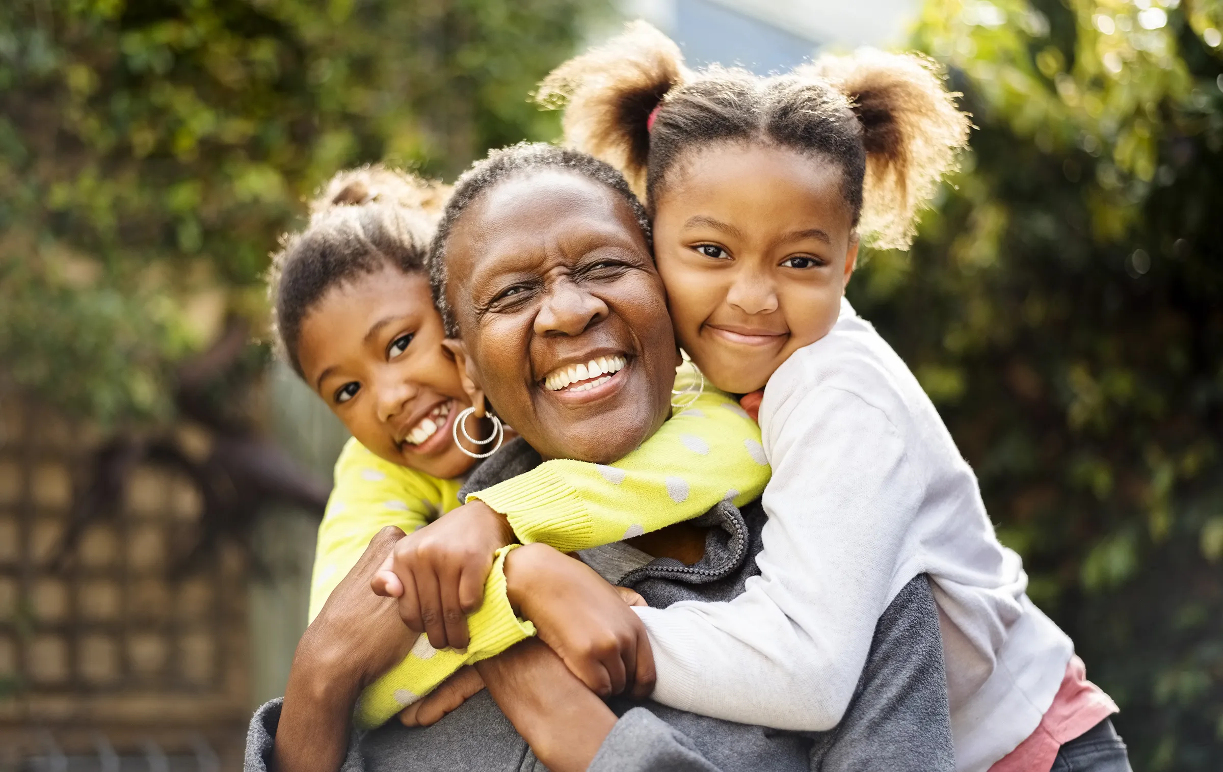 Grandmother hugging two smiling grandchildren outdoors