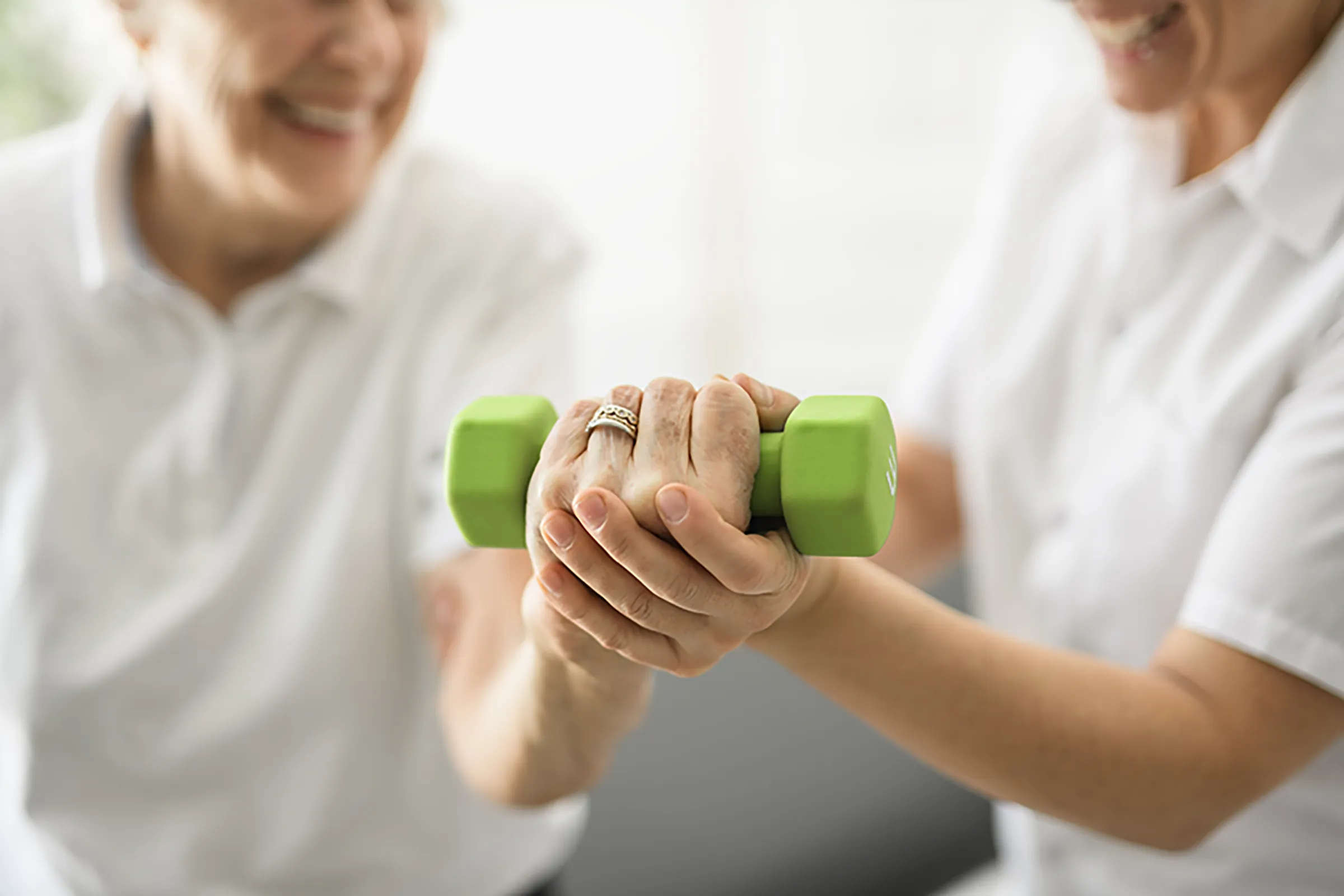 Senior lifting green dumbbell with caregiver support