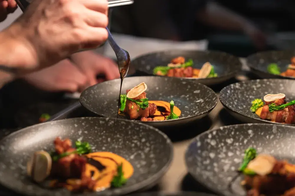 Chef drizzles sauce over gourmet plated dishes